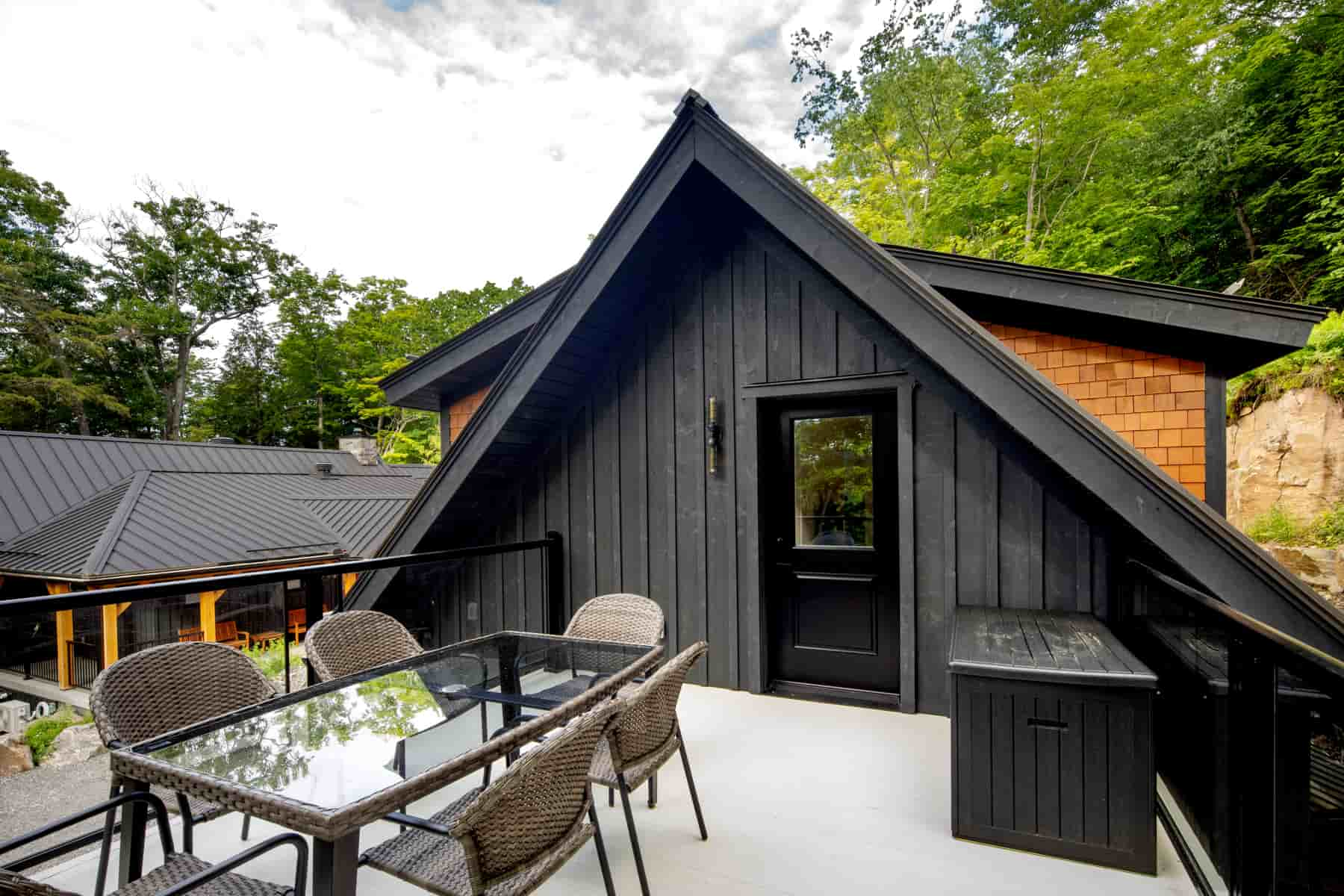  A modern black house with a deck and patio, overlooking the serene waters of Lake Muskoka, crafted by Ballantyne Builds.