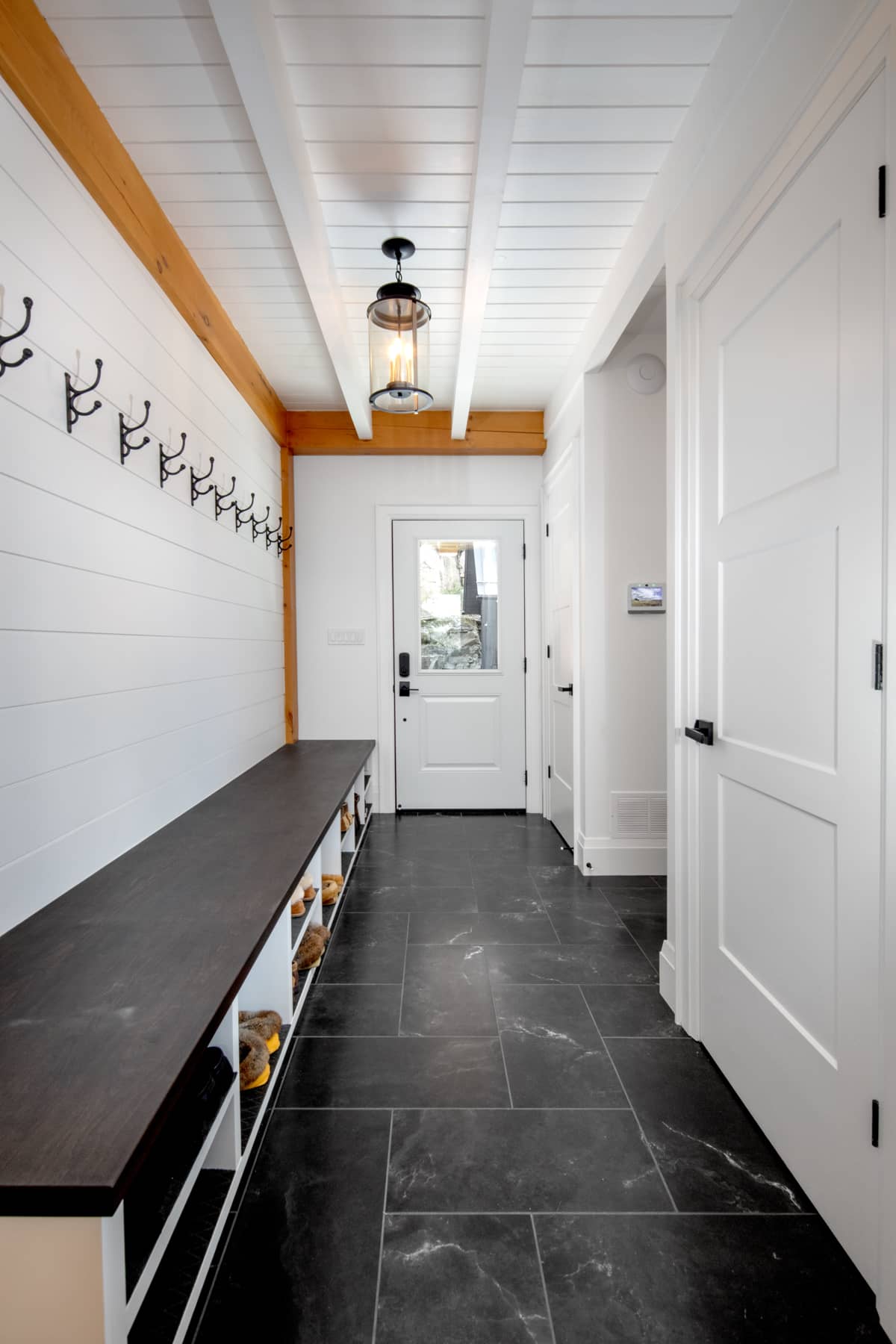  A mud room featuring white walls and a black tile floor, designed by Lake Muskoka Ballantyne Builds.