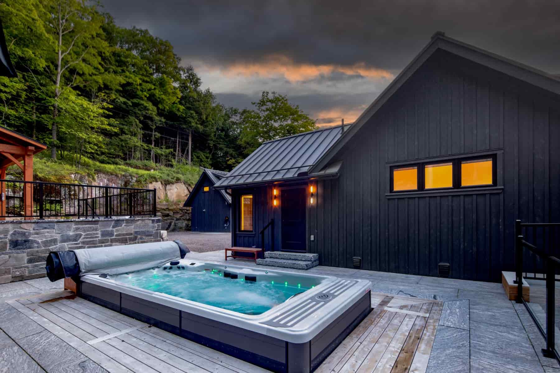 A luxurious hot tub positioned on a deck, with a sleek black house in the background, located at Lake Muskoka by Ballantyne Builds.
