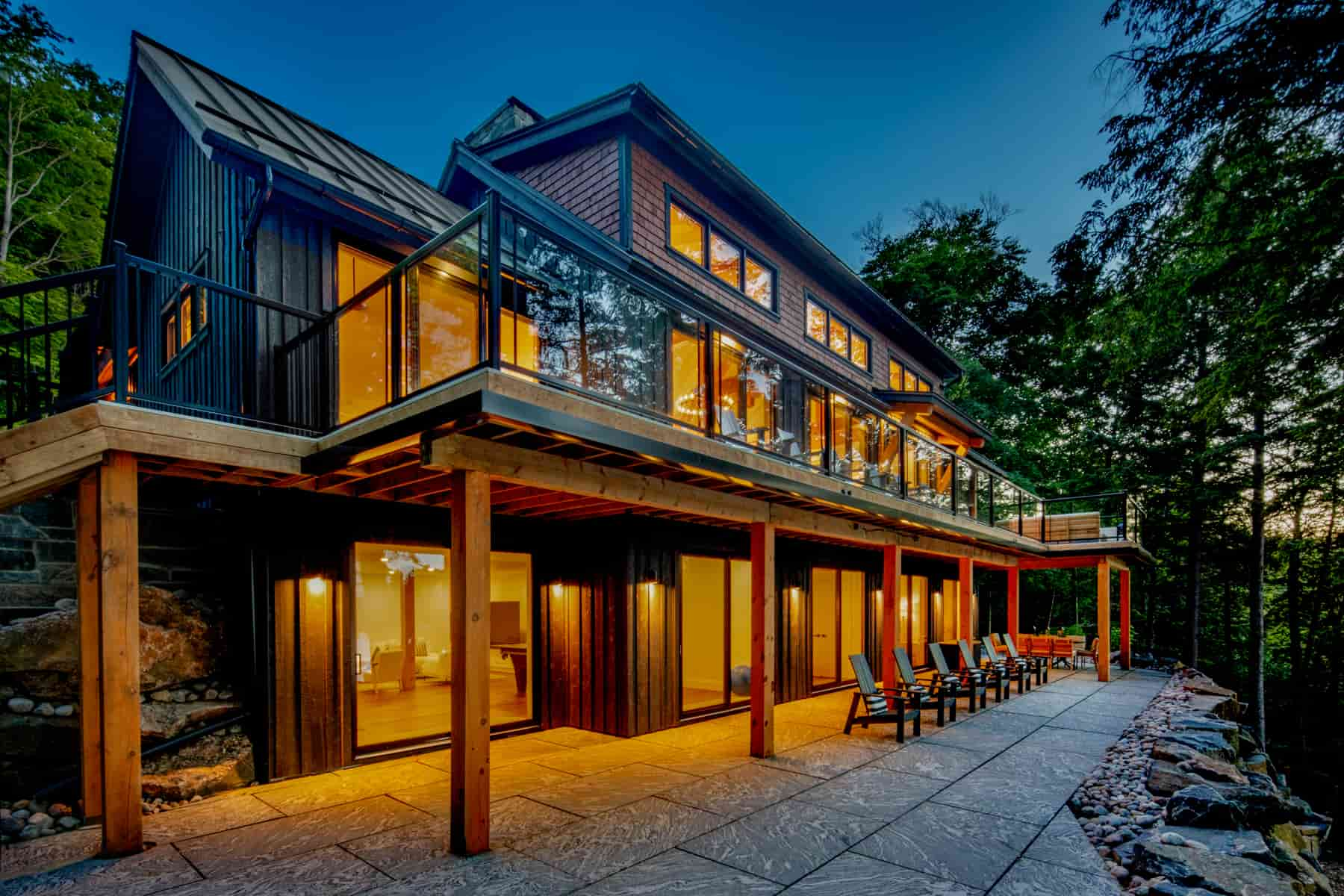 A stylish modern residence with a deck and patio, overlooking the serene waters of Lake Muskoka, crafted by Ballantyne Builds.